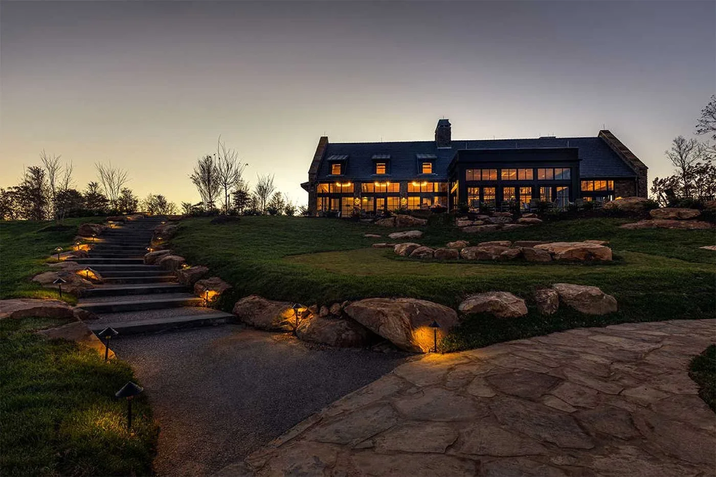 Lodge with glowing windows on a hillside above lit stone steps at dusk